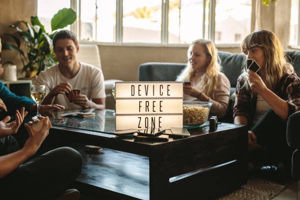 🤝 Building Community Through Offline Connections: Real-World Ways to Unplug and Reconnect Group of friends playing cards indoors at device free zone. Cell phones on table with young men and woman hanging out together.