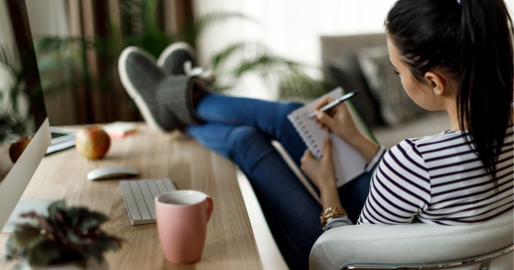 A woman taking a break from her computer, stretching with her arms overhead in a bright, peaceful workspace — symbolizing digital detox strategies and improved work-life balance.