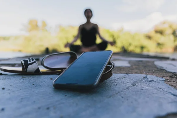 A person practicing meditation outdoors with a smartphone placed nearby, symbolizing mindful unplugging and the benefits of a digitaldetox.