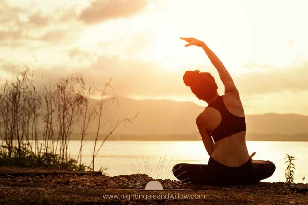 Blog A person peacefully stretching by a calm lake at sunrise, representing unplugging routines to reduce stress through mindful movement and connection with nature.