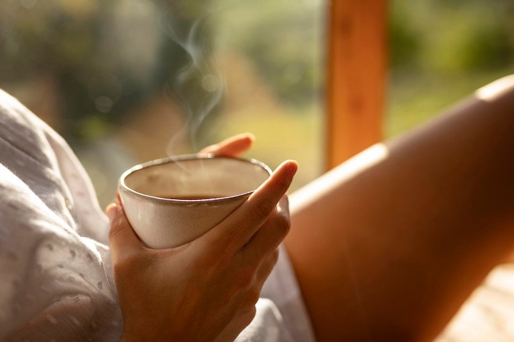 Blog Close-up of hands holding a steaming coffee cup in warm morning sunlight, symbolizing how to incorporate unplugging into your daily life with calm and mindful presence.