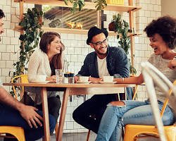 A diverse group of friends laugh together at a cafe, connecting in person over coffee instead of checking their phones, as part of a healthy digitaldetox routine .
