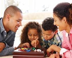 A happy family participating in a family-friendly digital detox activity by playing a board game together at their dining table, laughing and connecting without screens.