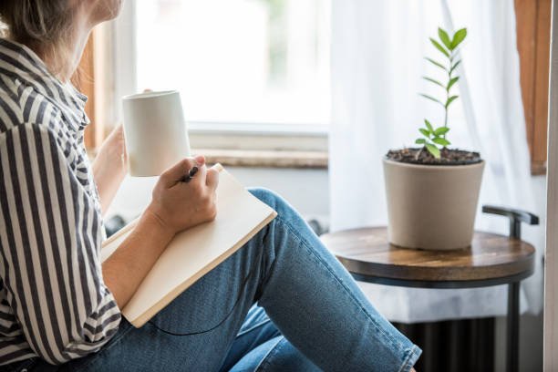 A person starting their day with a mindfulness practice of journaling next to a window with a warm drink, creating a peaceful and intentional morning routine.