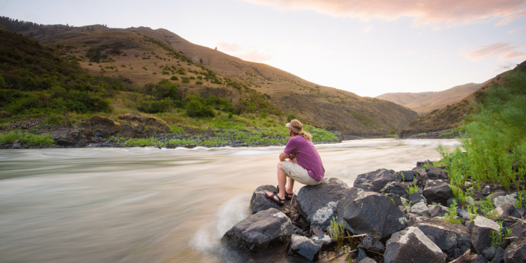 Blog Person seated by a tranquil lakeside at sunset, embodying the long-term benefits of unplugging for mental clarity, relaxation, and emotional restoration.