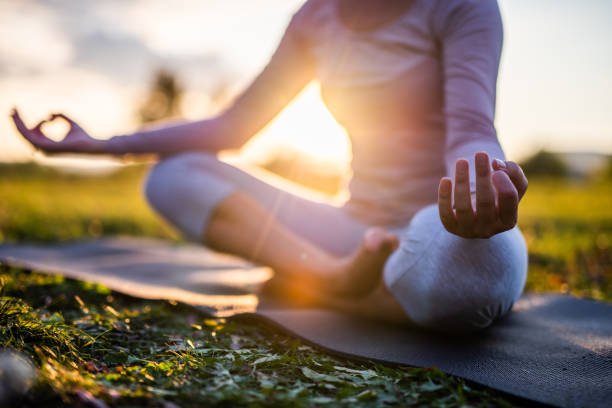 Blog Illustrating the serene result of a daily mindfulness practice: a woman meditates peacefully on a yoga mat in a grassy field, bathed in the warm, golden light of sunset.