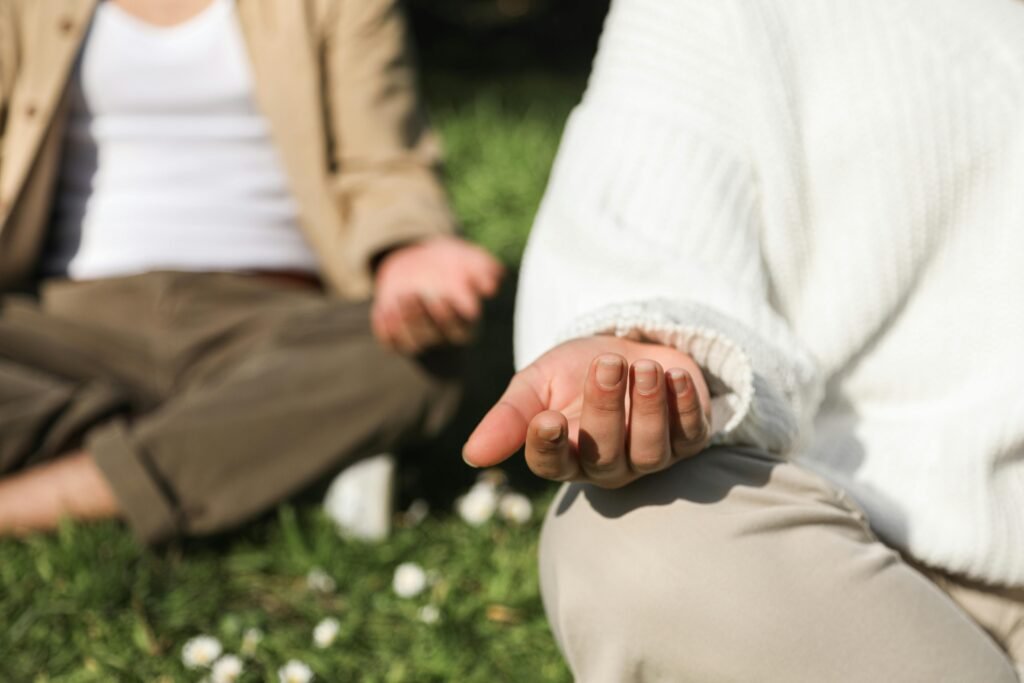 Two people practice mindfulness meditation outdoors on the grass, illustrating the powerful mind-body connection for mental and physical health.