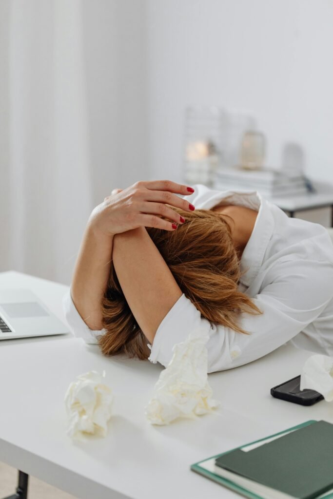 A stressed woman with her head in her arms on an office desk with tissues, illustrating the need for mental wellness during challenging times.