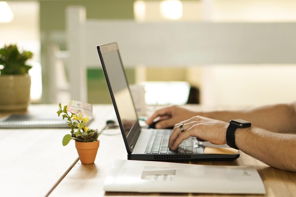 Blog Side view of a person working on a laptop in an office, with their hands on the keyboard and trackpad.