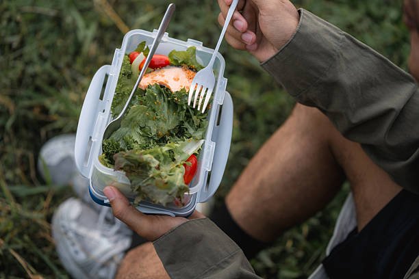 7 Thrilling Sustainable Living Challenges to Try This Month: Your Eco-Adventure Awaits! A young man sits on a blanket in a park, enjoying a solitary picnic with a basket of fresh fruit and healthy food.