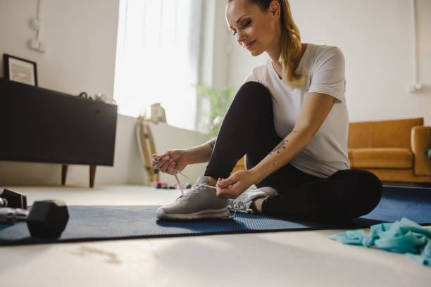 The Motivation Reset: How to Stay Motivated with Home Workouts for Good A woman shows how to stay motivated with home workouts by smiling as she ties her running shoes, getting ready for her fitness routine in her living room.
