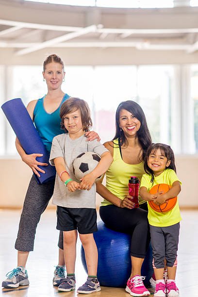 A group of mothers in a fitness class demonstrating a fun family-friendly fitness schedules by exercising on mats with their children.