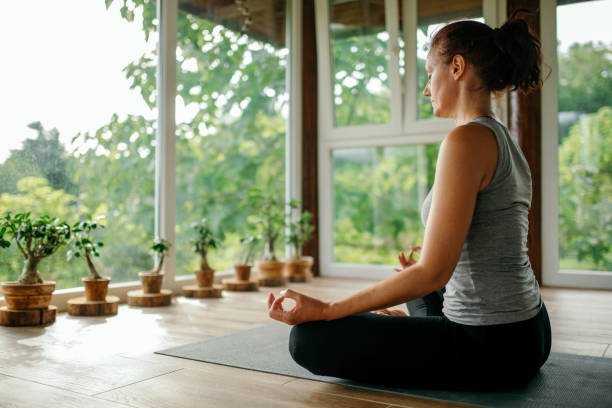 A mature woman integrates meditation and mindfulness into her exercise routine by practicing yoga on a mat on her home terrace.