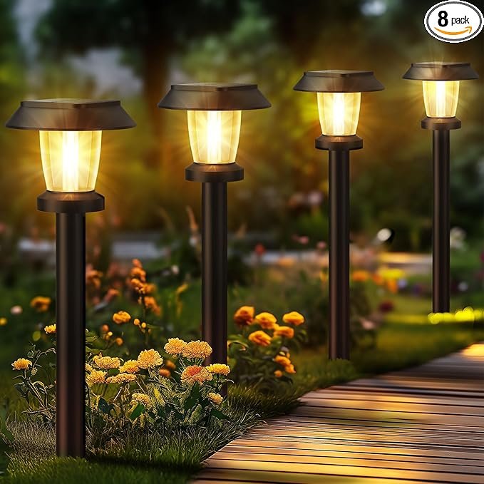 Solar lighting ideas for eco gardens: A set of 8 bronze solar-powered stake lights illuminating a garden pathway with a warm, patterned glow at dusk.