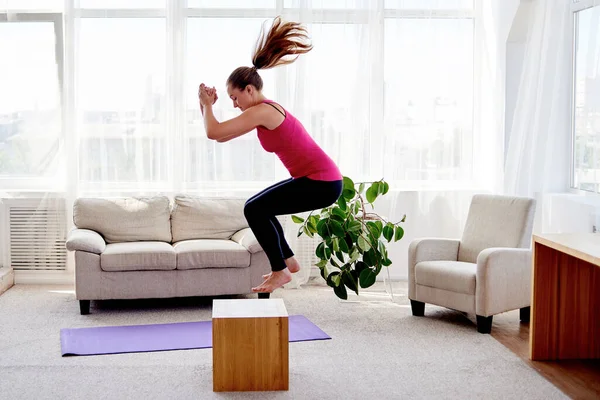 A woman performs a powerful jump squat as part of an intense at-home HIIT workouts.