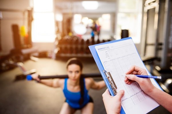 A woman in workout clothes consulting her weekly home workout schedules on a tablet before starting her exercise routine.